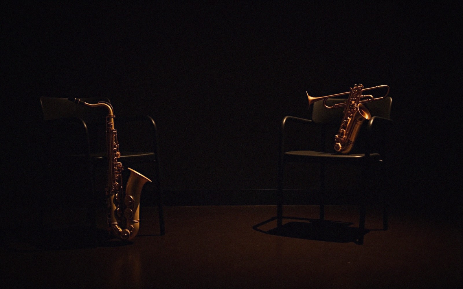 Saxophones and a trumpet rest on empty chairs on a dimly lit stage